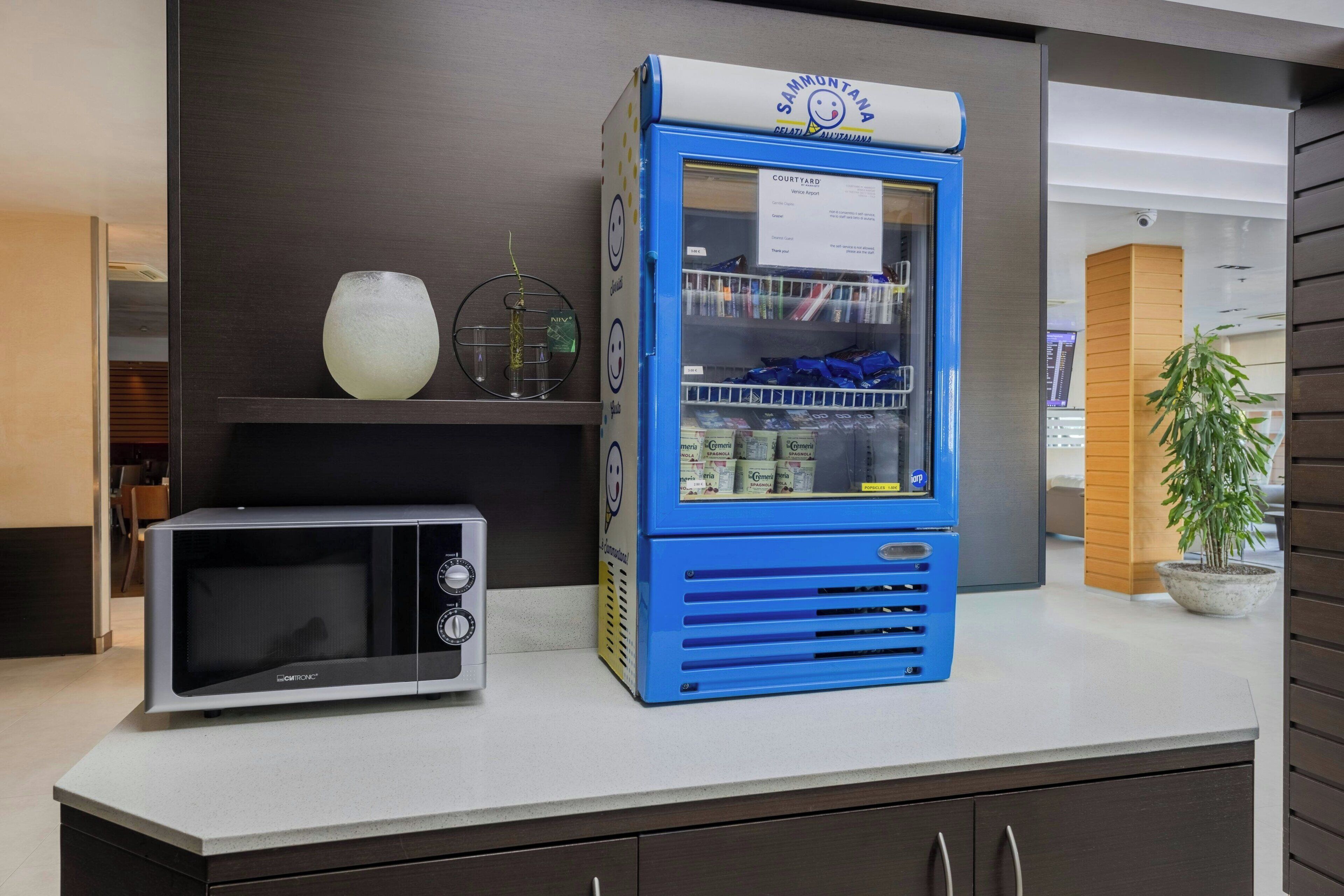 A kitchen area with a microwave and a blue vending machine.