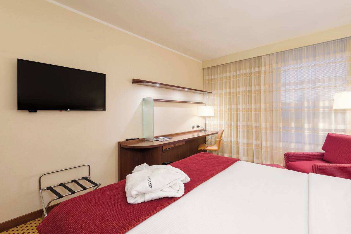 Une chambre d’hôtel avec un lit, un bureau, une chaise, une télévision et une fenêtre avec des rideaux.