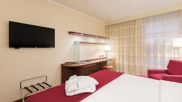 Una habitación de hotel con cama, escritorio, silla, televisor y ventana con cortinas.