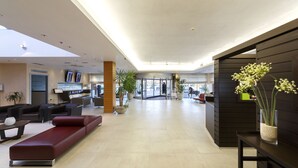 Een moderne lobby met een receptiebalie, een zithoek en potplanten.