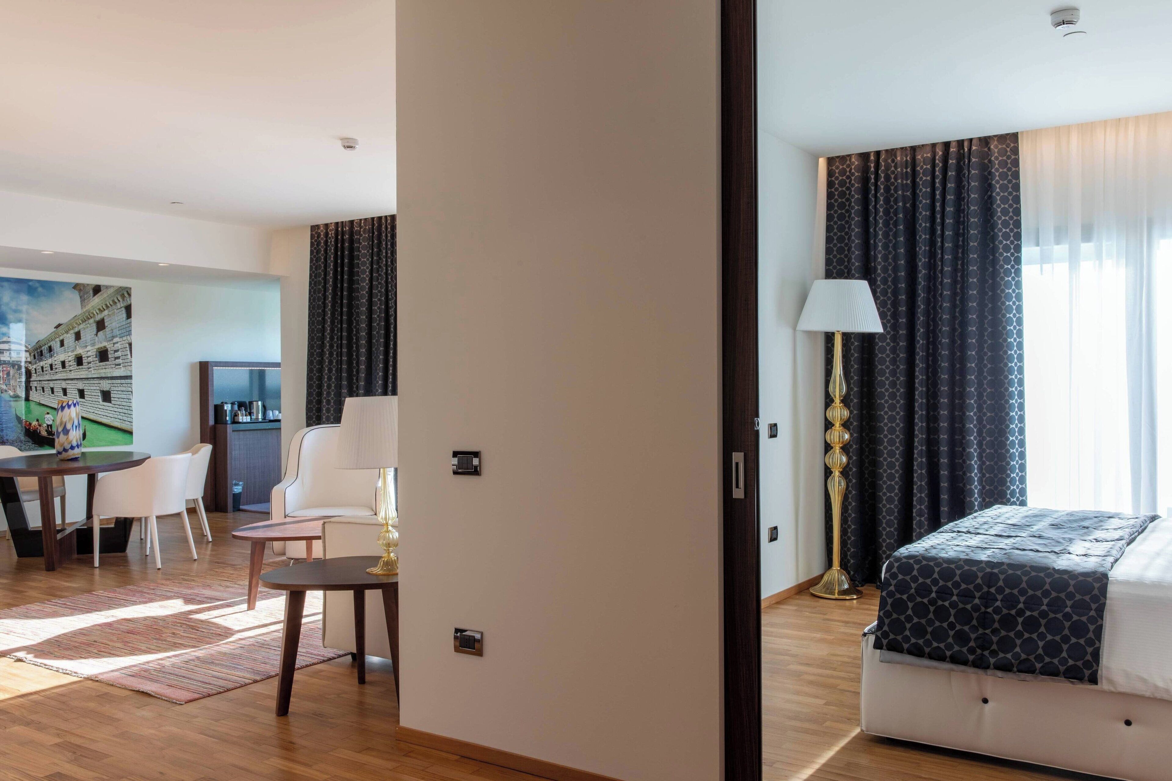 Habitació d'hotel amb llit, escriptori amb cadira, làmpada i un quadre a la paret.