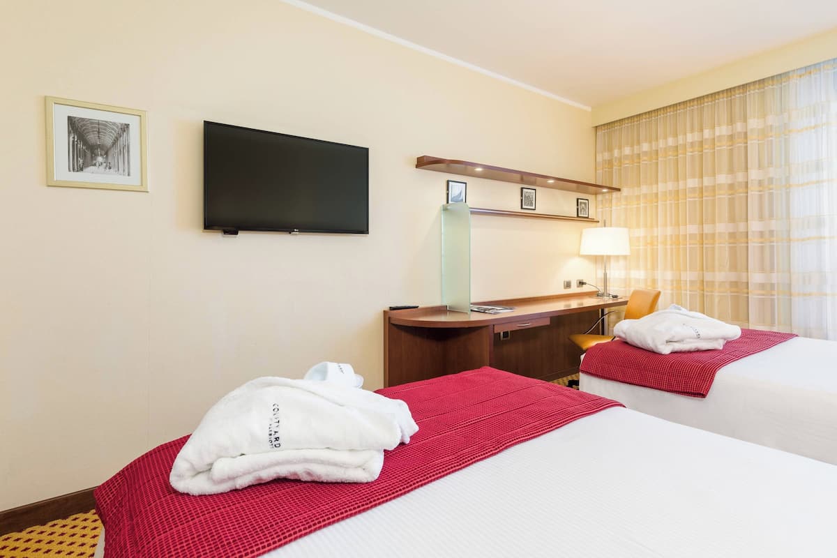 Une chambre d’hôtel avec deux lits, un téléviseur à écran plat, un bureau et une fenêtre avec des rideaux.