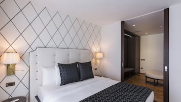 A modern hotel room with a neatly made bed, two bedside lamps, a wall-mounted light fixture, and a wooden floor.