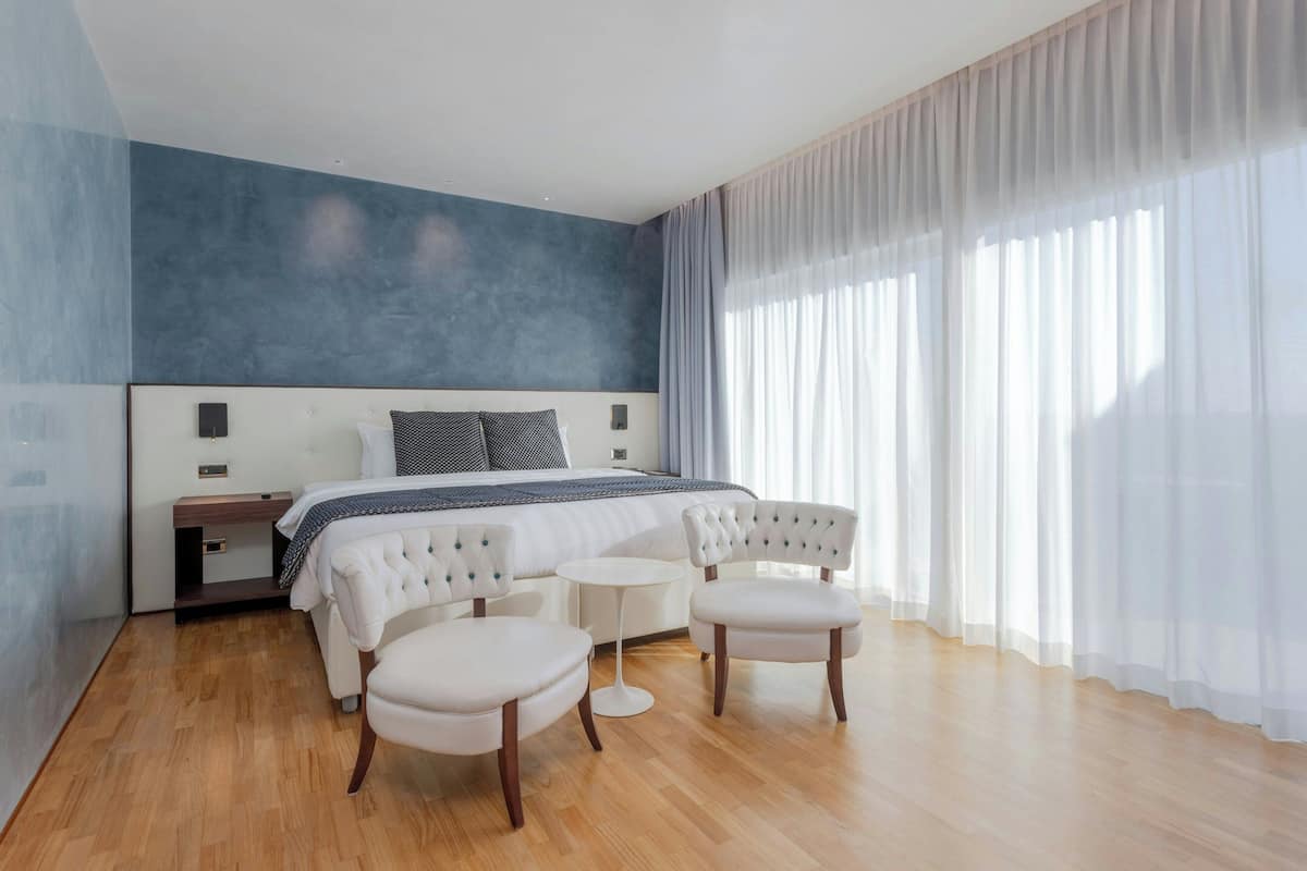 Une chambre à coucher moderne avec un grand lit, deux fauteuils blancs, une petite table ronde et une table de chevet.