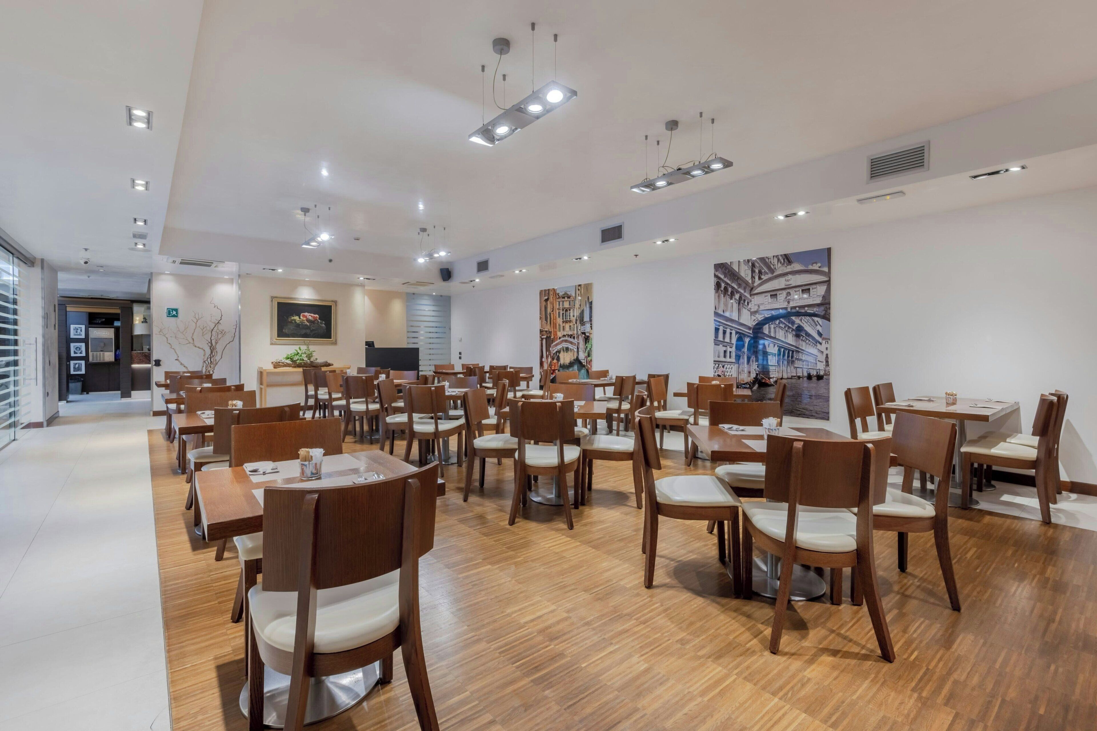A spacious dining area with multiple tables and chairs, a modern ceiling design with recessed lighting, and a large mural on the wall.