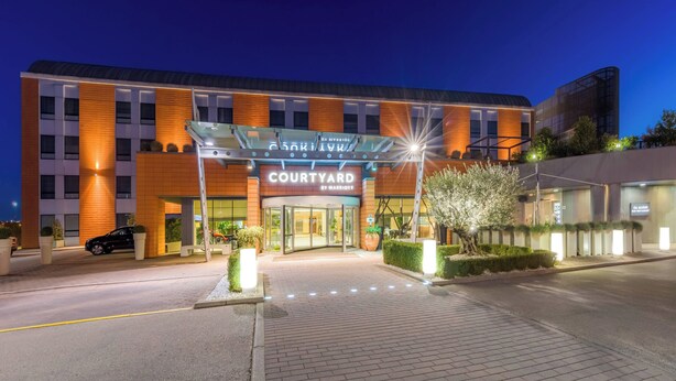 Entree van een Courtyard by Marriott hotel in de schemering, met een modern ontwerp, glazen ingang en een goed verlicht pad.