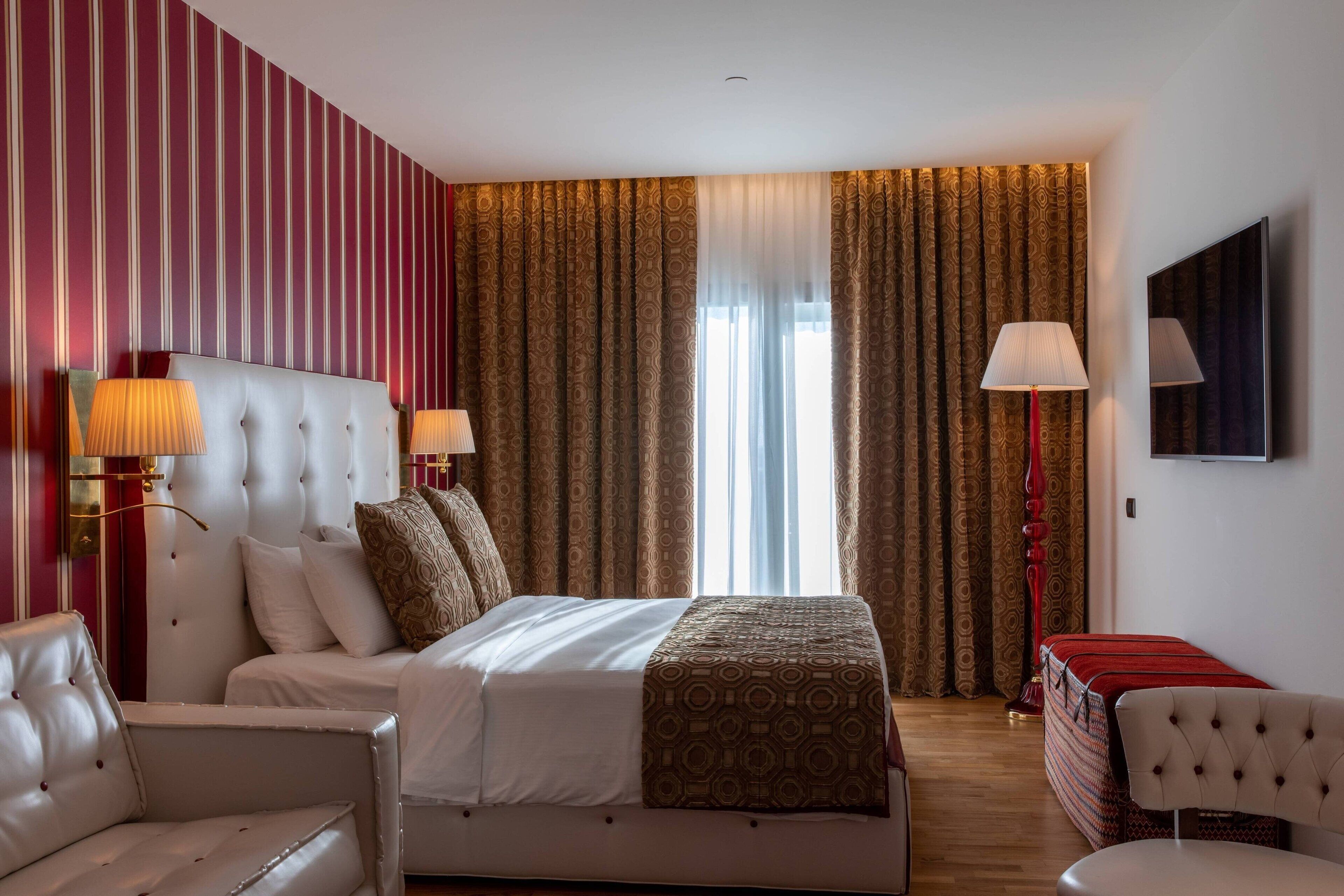 Ein Hotelzimmer mit einem großen Bett, zwei Nachttischen mit Lampen, einem an der Wand montierten Fernseher und einer rot-weiß gestreiften Wand.