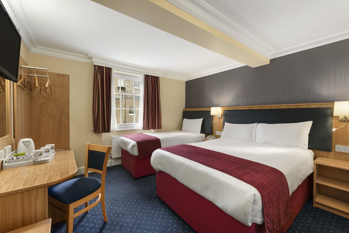 A hotel room with two beds, a desk, a chair, a TV, and a window with curtains.