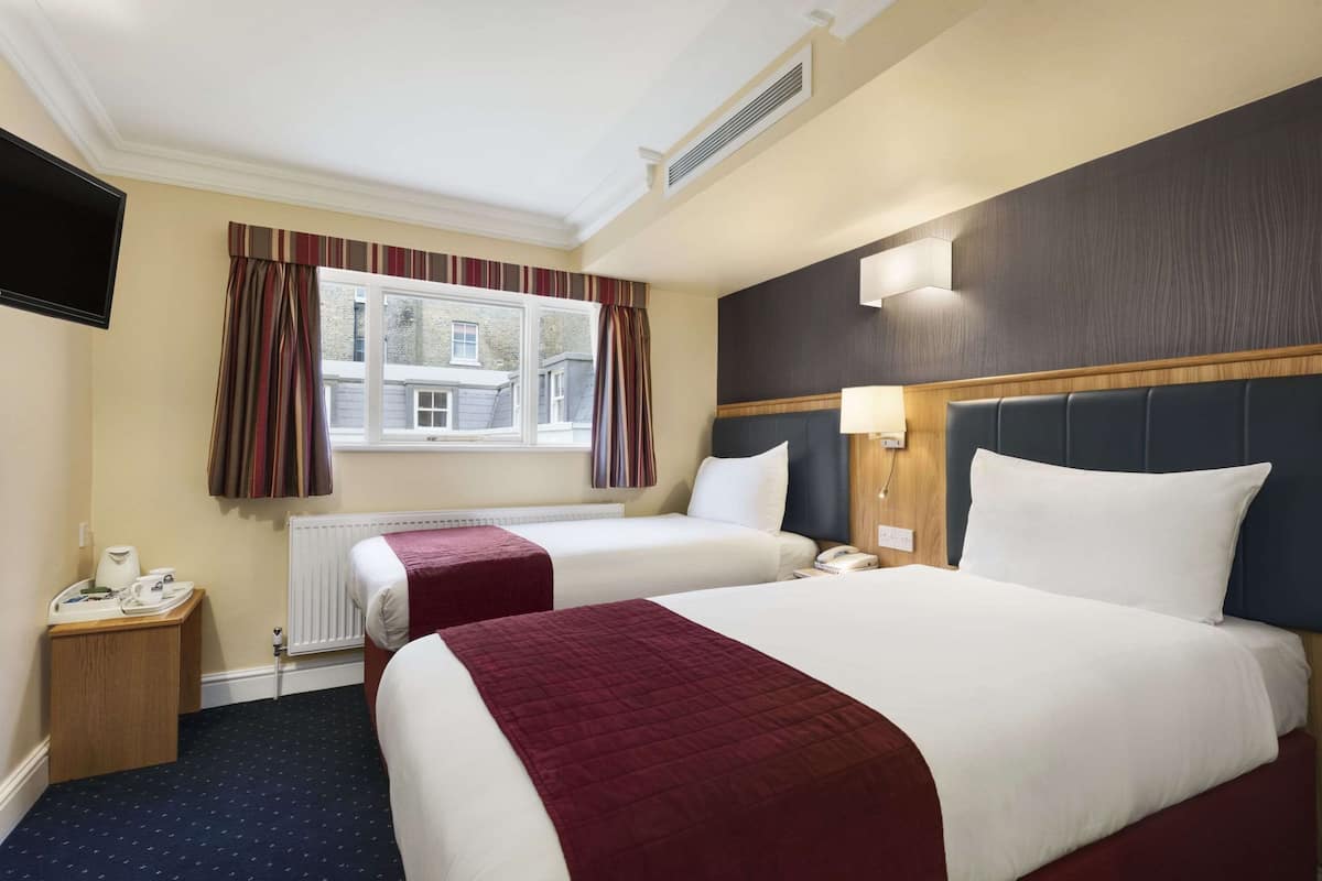 A hotel room with two beds, a TV, a desk with a telephone, and a window with curtains.