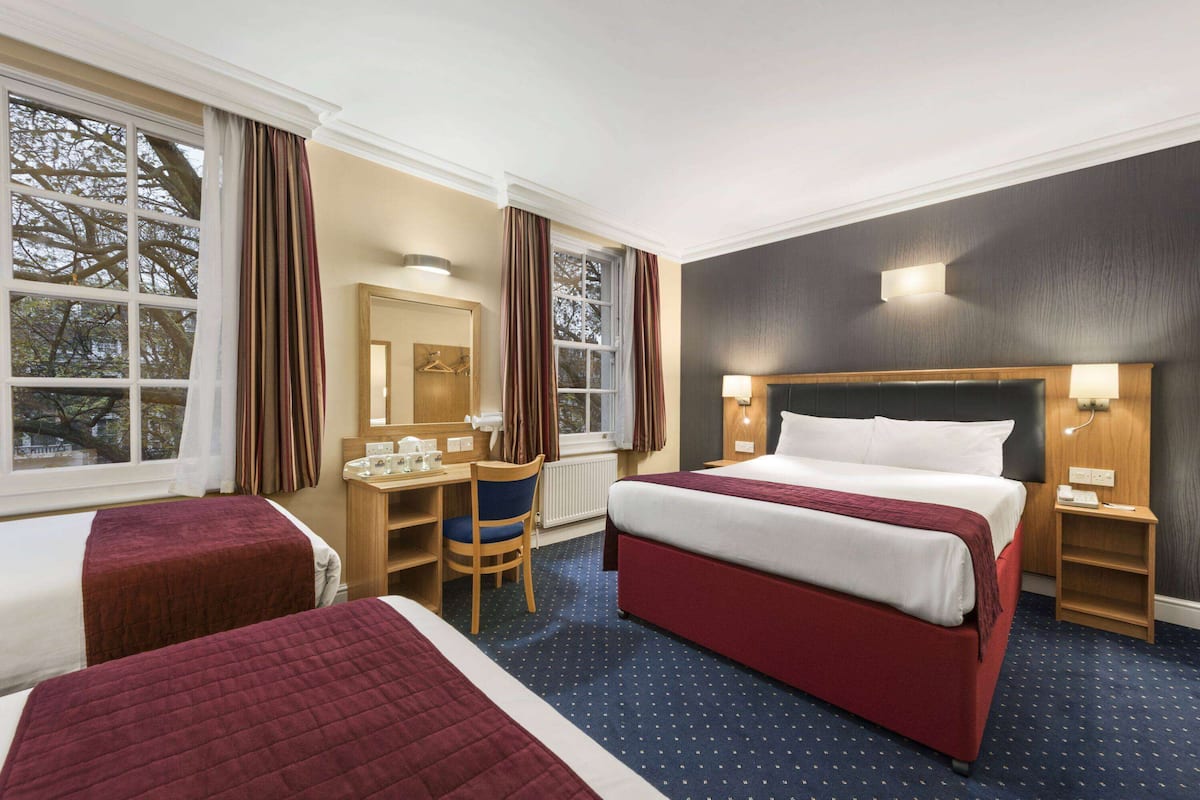 A hotel room with two beds, a desk, a chair, a mirror, and a nightstand.