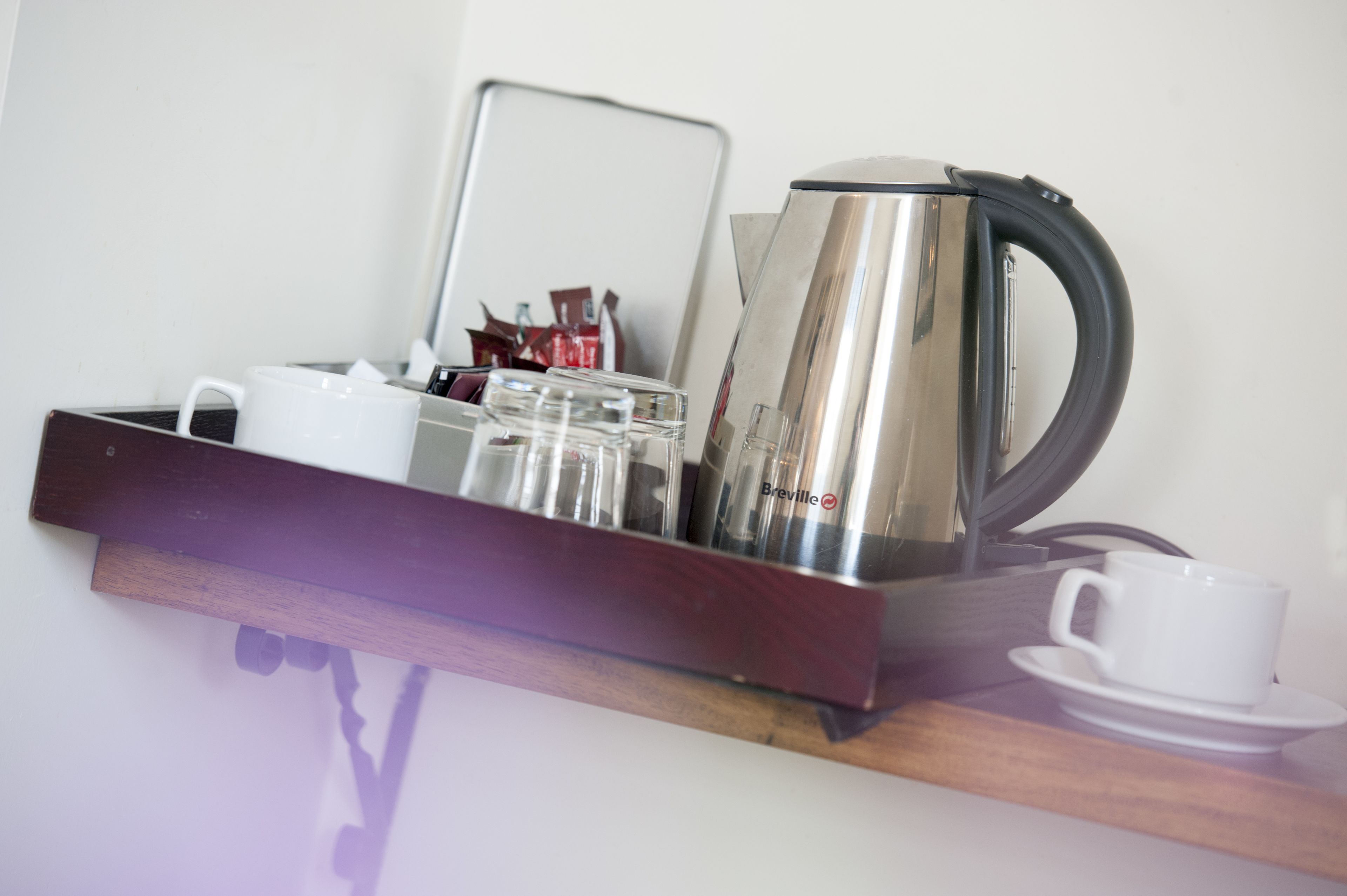 A tray with a Breville coffee maker, a white mug, and a glass set on a wooden shelf.