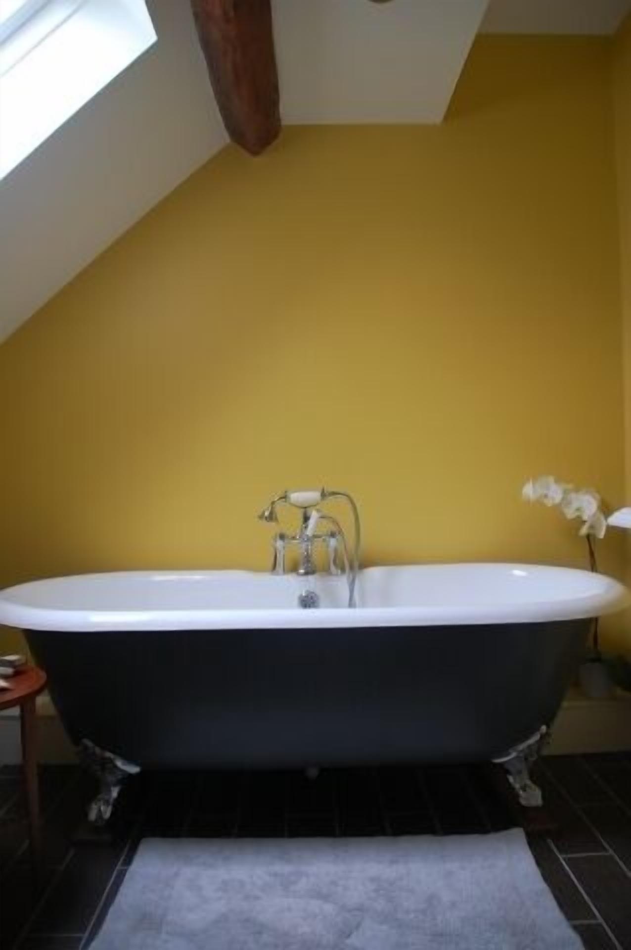 A bathroom with a freestanding bathtub, a small wooden stool, and a potted orchid.