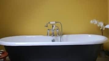 A bathroom with a freestanding bathtub, a small wooden stool, and a potted orchid.