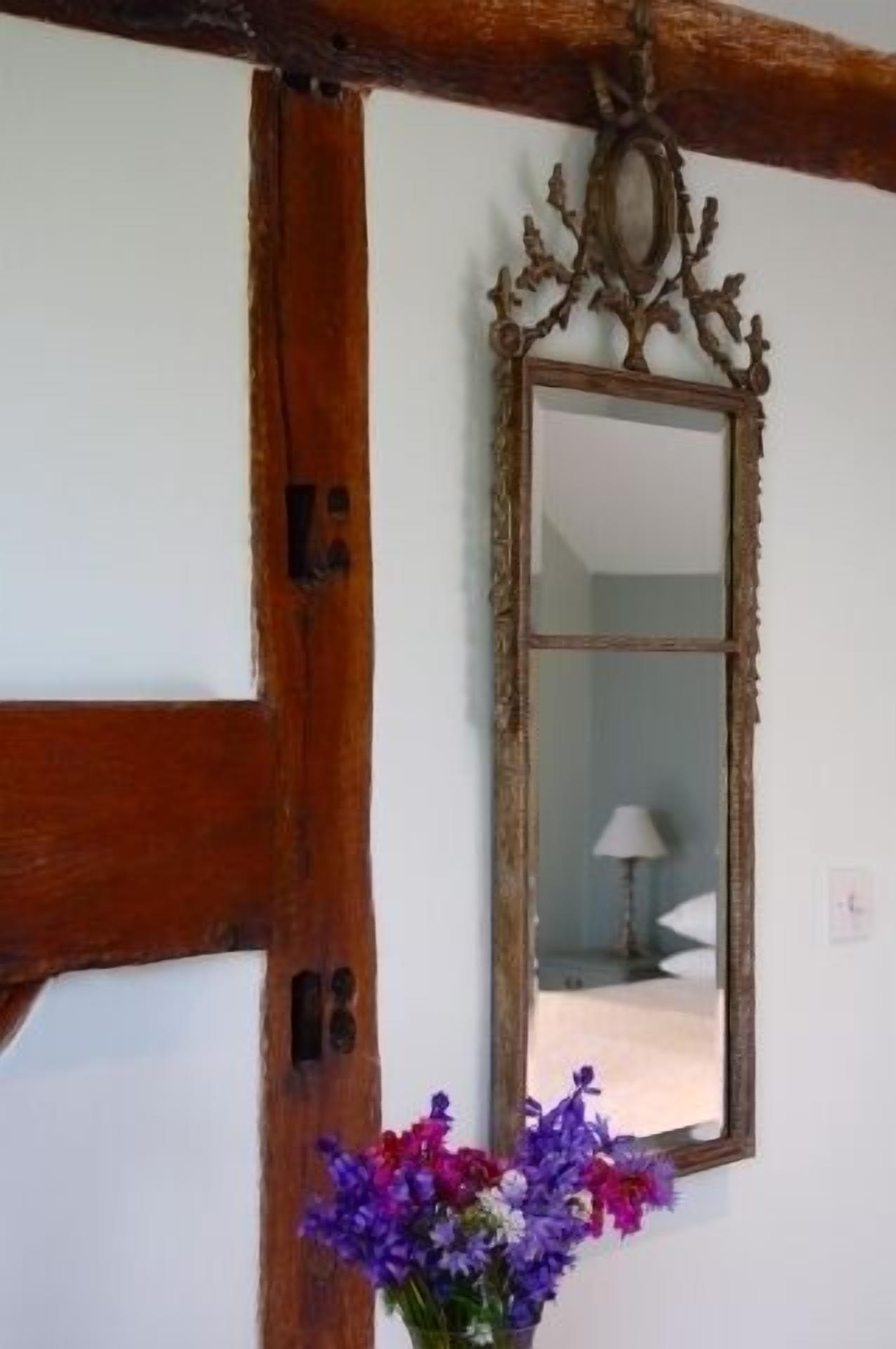 A room with a wooden beam ceiling, a mirror with an ornate frame, and a vase of purple flowers.