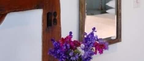 A room with a wooden beam ceiling, a mirror with an ornate frame, and a vase of purple flowers.
