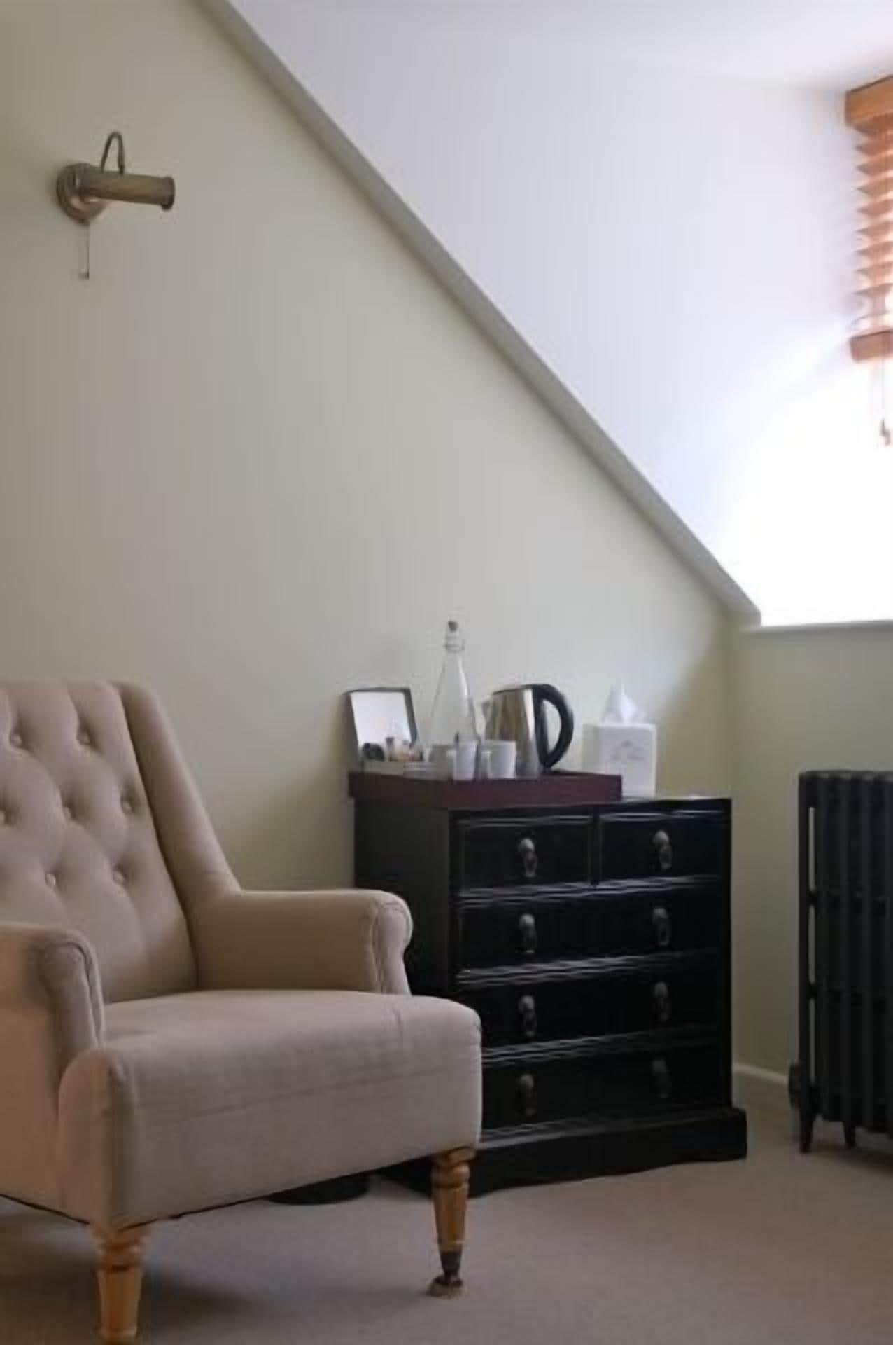 Une pièce comprenant un fauteuil capitonné, une commode en bois foncé dotée de tiroirs et un radiateur.