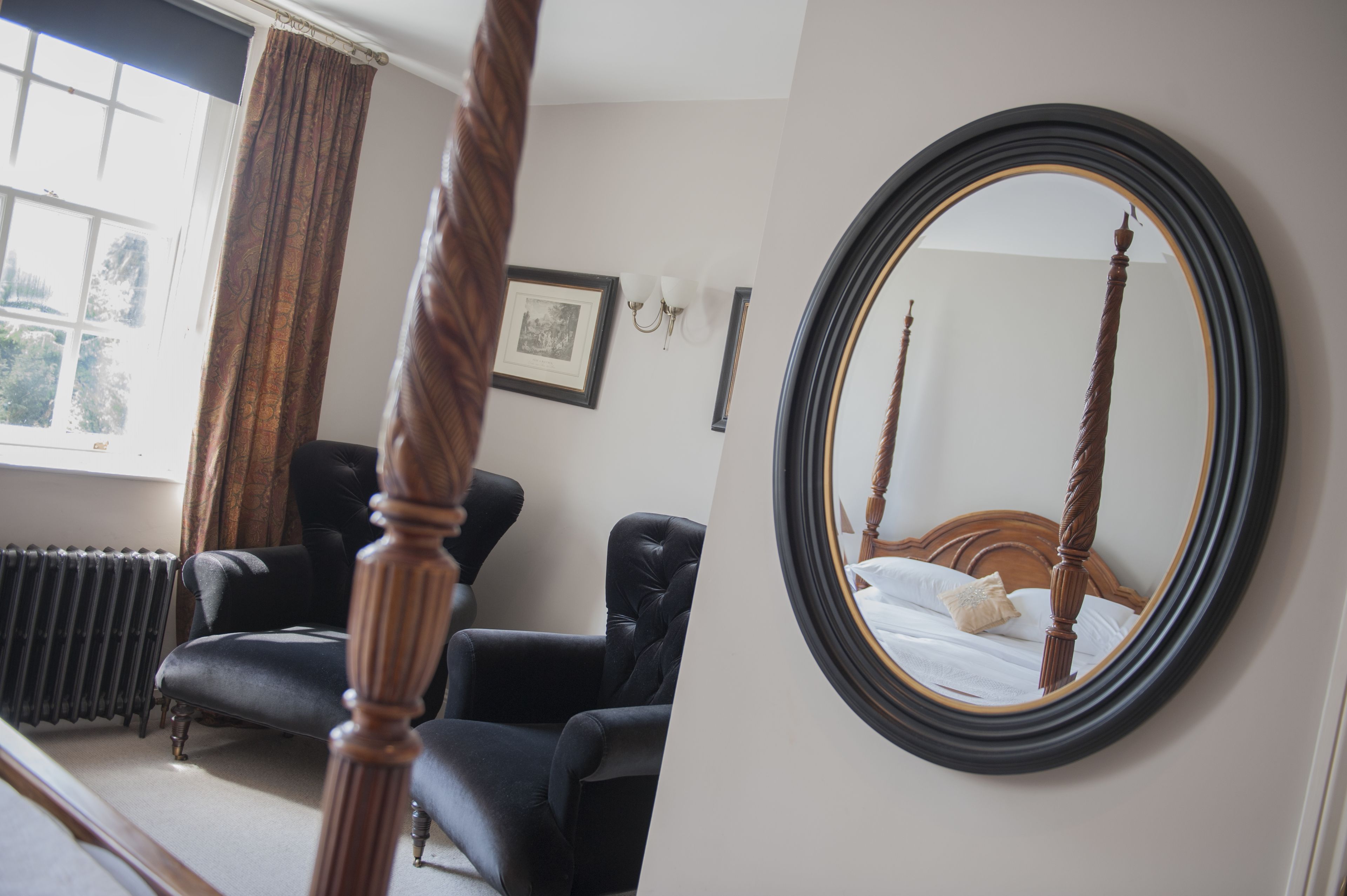 A bedroom with a four-poster bed, a black leather armchair, a radiator, and a framed picture on the wall.