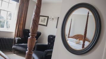 Un dormitorio con una cama con dosel, un sillón de cuero negro, un radiador y un cuadro enmarcado en la pared.