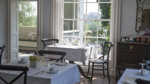 Un comedor con una mesa lista para dos personas, una silla, un armario de madera y una ventana con vistas a la vegetación.