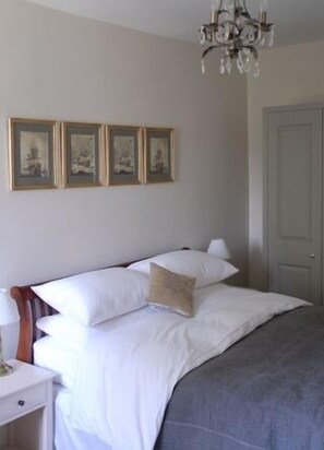 A neatly made bed with white linens and a gray blanket, a wooden nightstand with a lamp, and three framed pictures on the wall. - The Bridge House Boutique B&B (Ross-on-Wye)