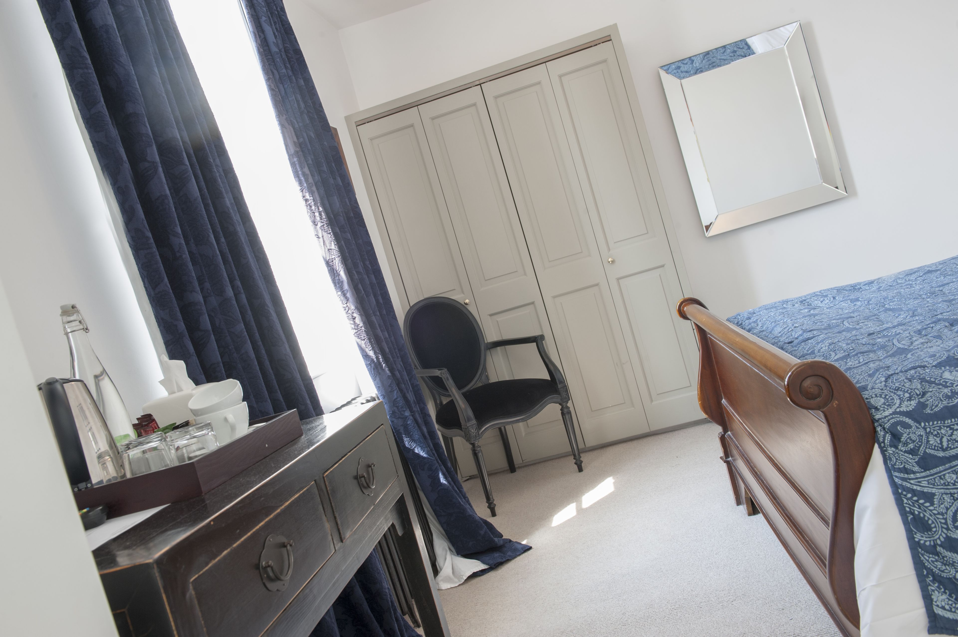 A bedroom with a bed, a dresser, a chair, a wardrobe, and a mirror.