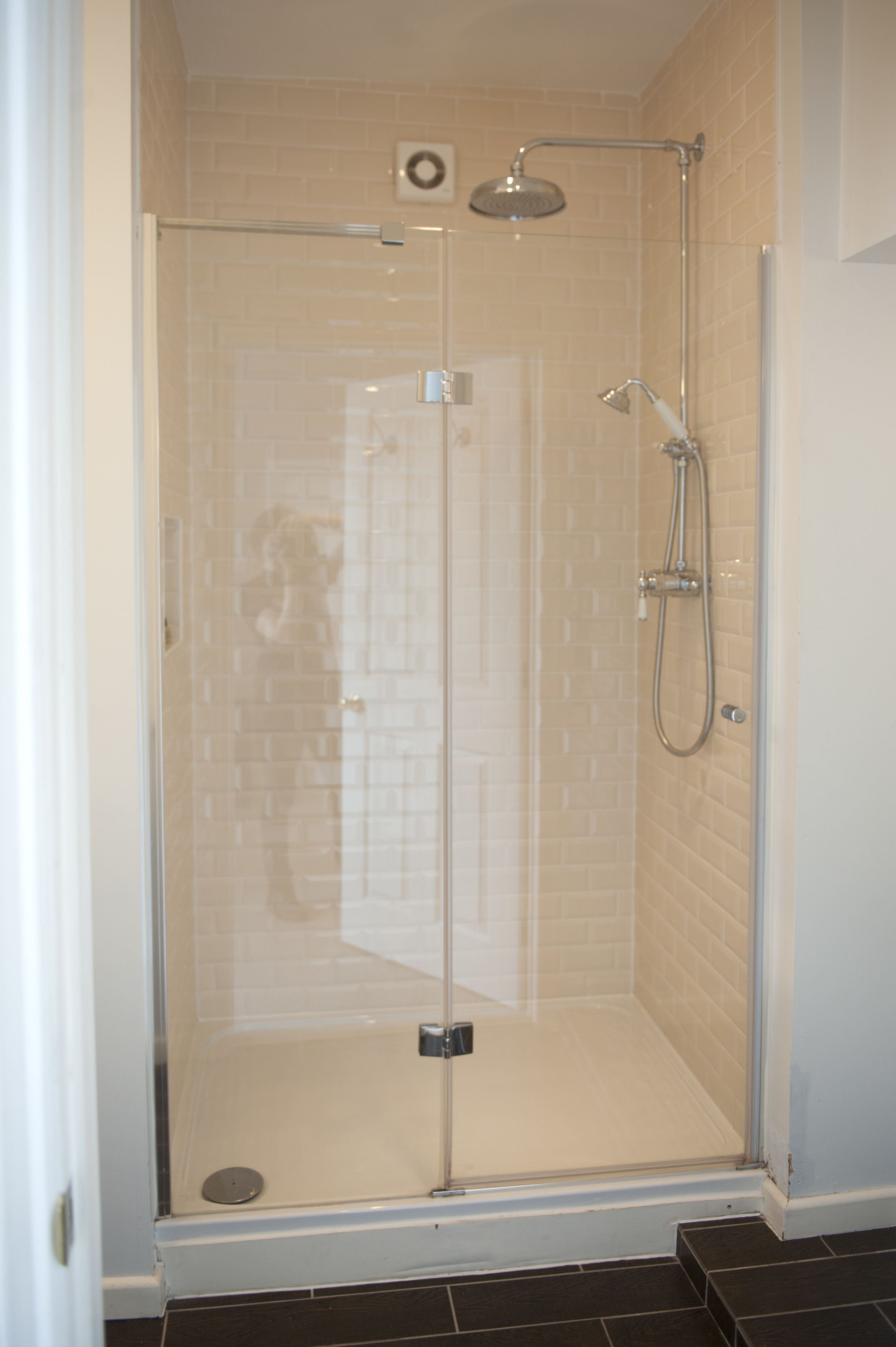 A glass-enclosed shower stall with a handheld showerhead and a wall-mounted faucet.