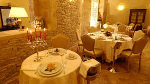 Uma sala de jantar com paredes de pedra, um candelabro com velas e uma mesa posta para refeição.