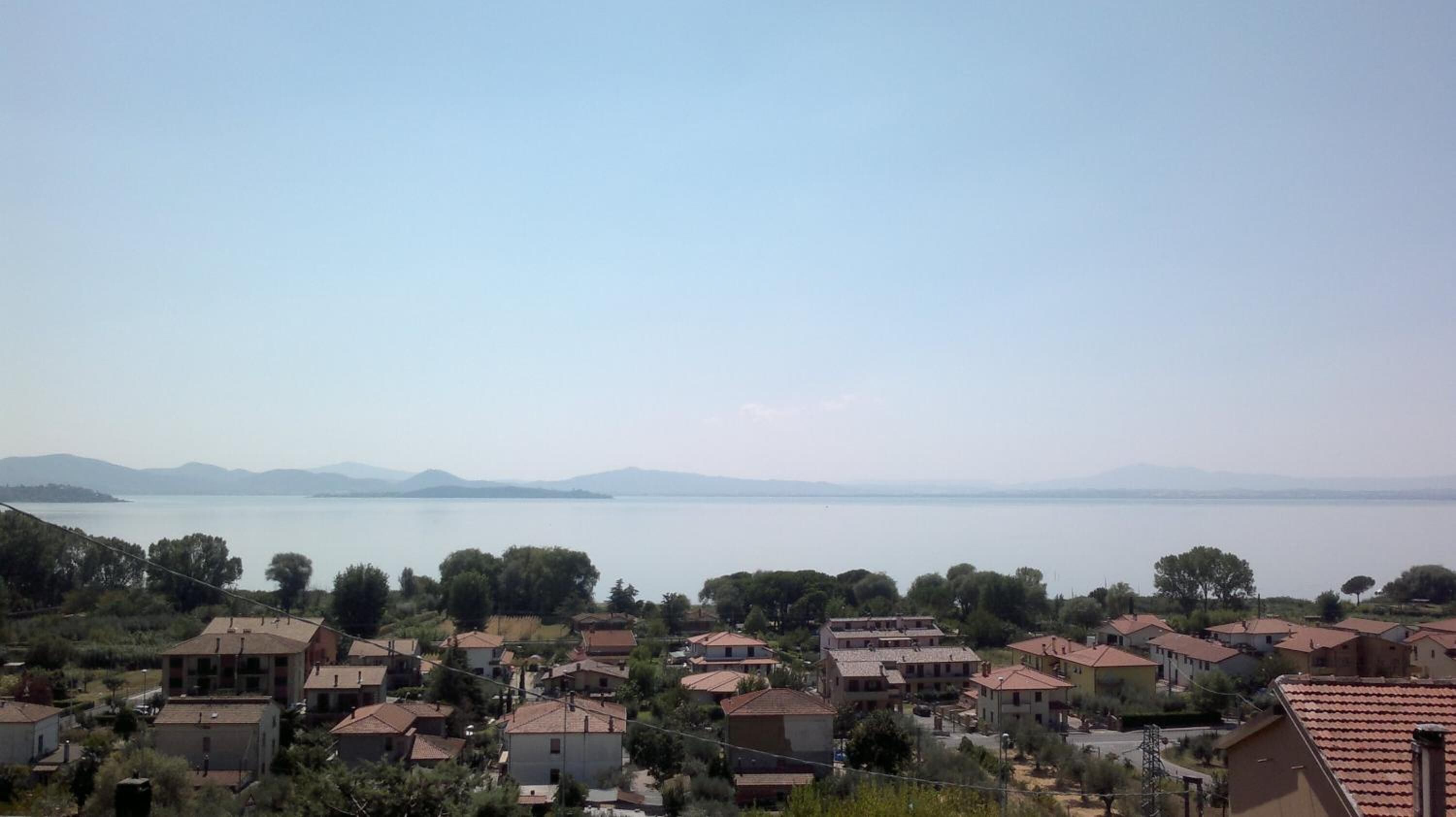 Ein Küstenwohngebiet mit Häusern, Bäumen und einem ruhigen Meer unter klarem Himmel.