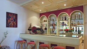 A bar area with stools, a coffee machine, and shelves with bottles. - Hotel Cavalieri (Passignano sul Trasimeno)