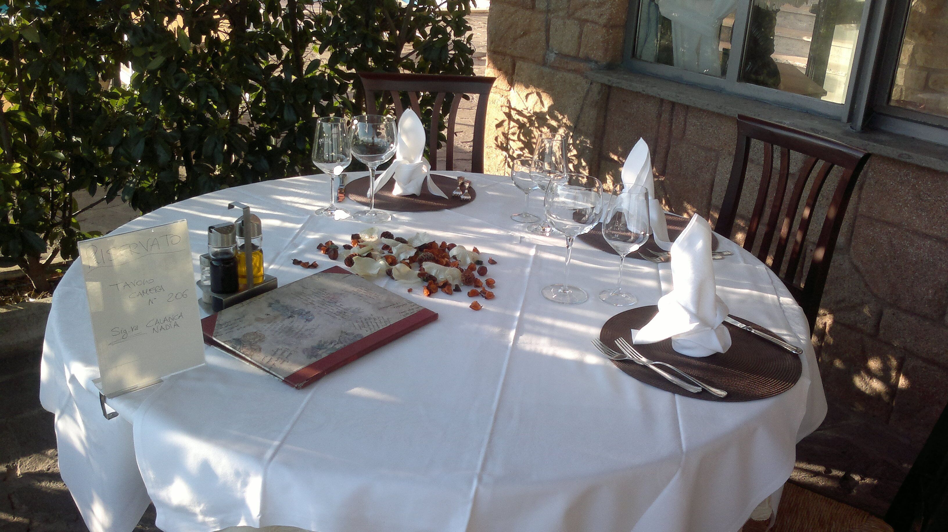 A table set for a meal outdoors with a menu, glasses, and cutlery.