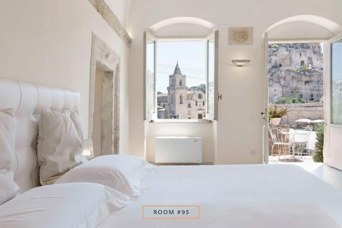 A hotel room with a large bed, a view of a historic building, and a balcony with outdoor furniture.