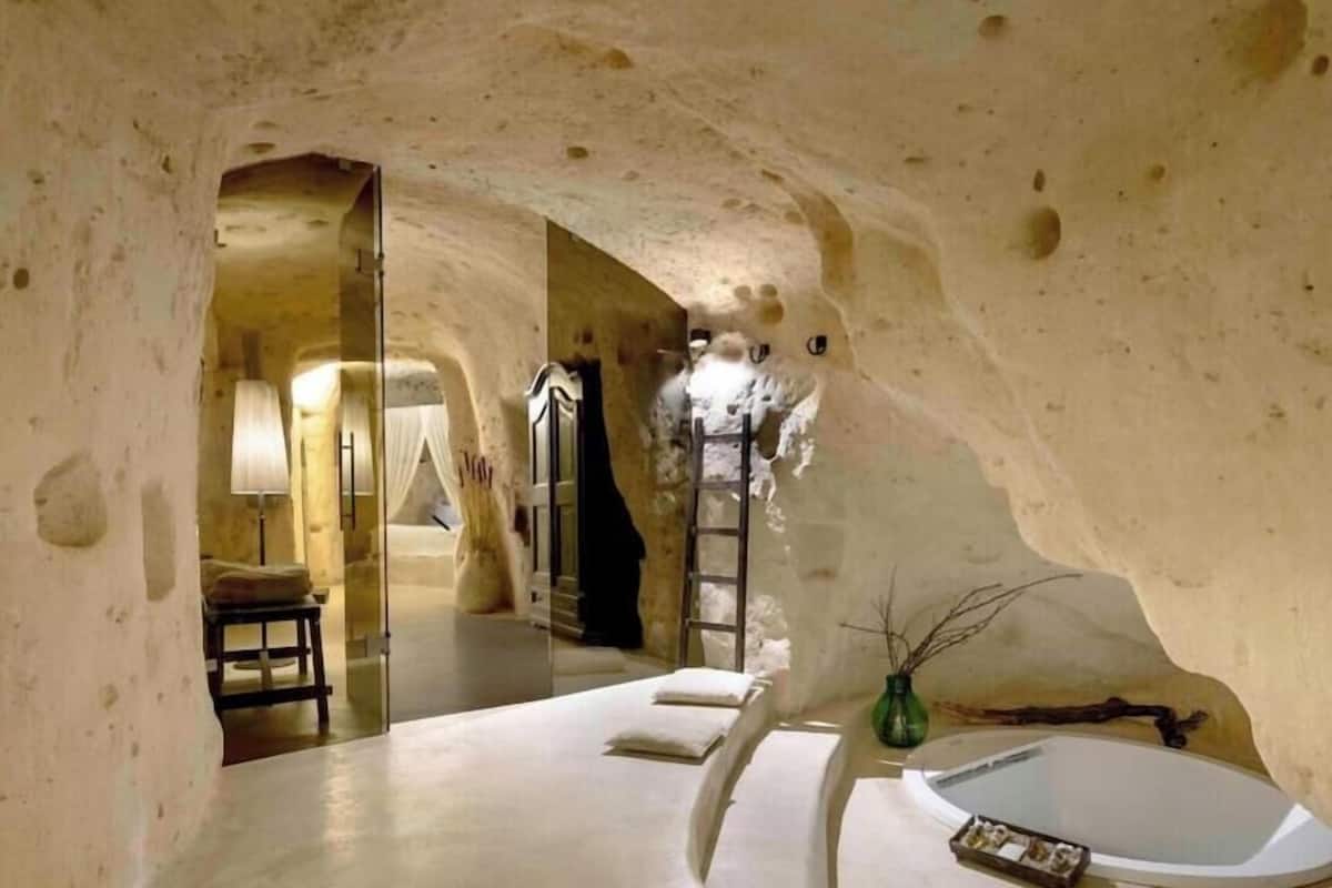 An interior with a stone wall, a bed, a bathtub, and a ladder.