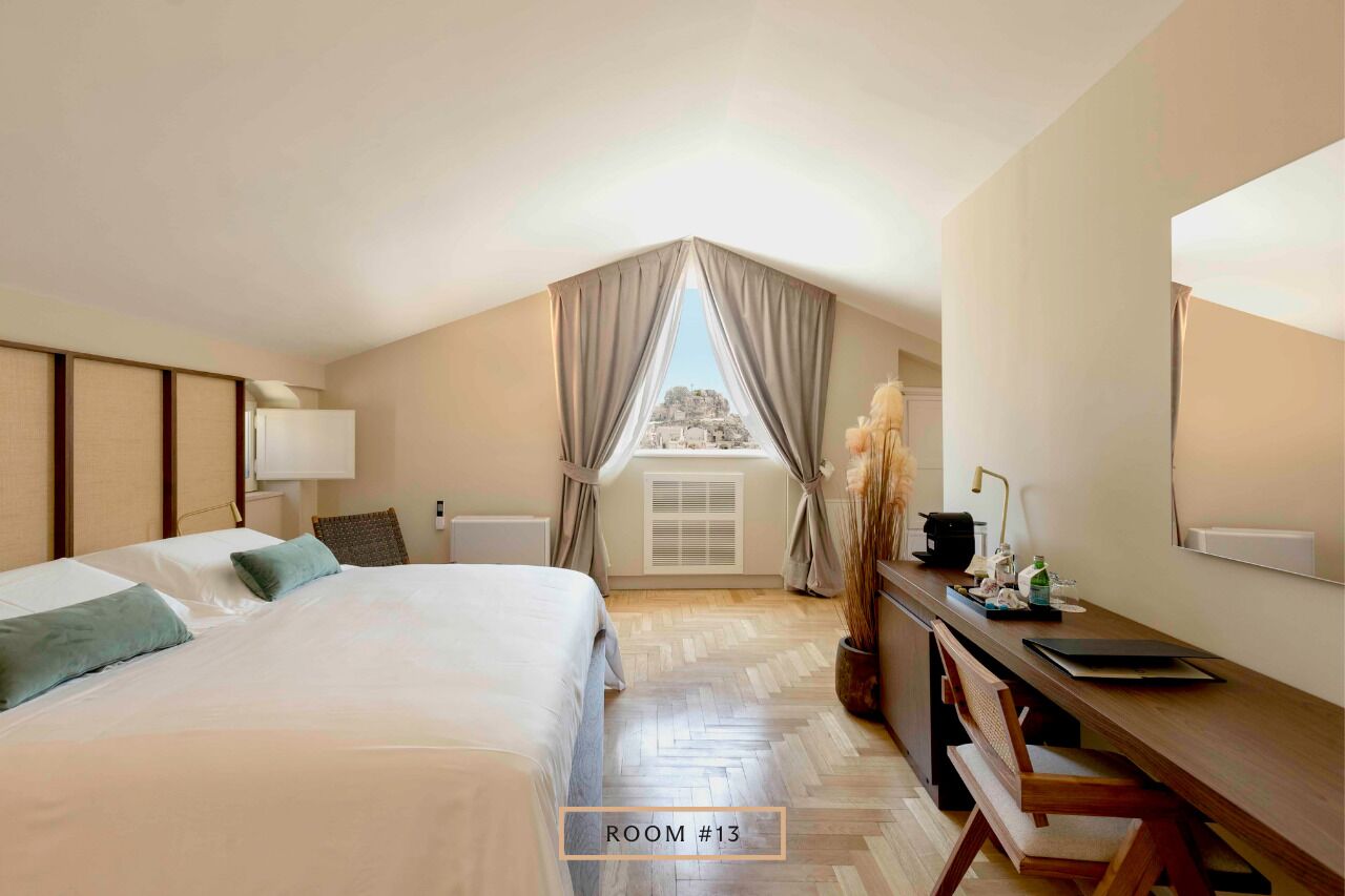 Un dormitorio con cama, escritorio, silla, lámpara y ventana con cortinas.
