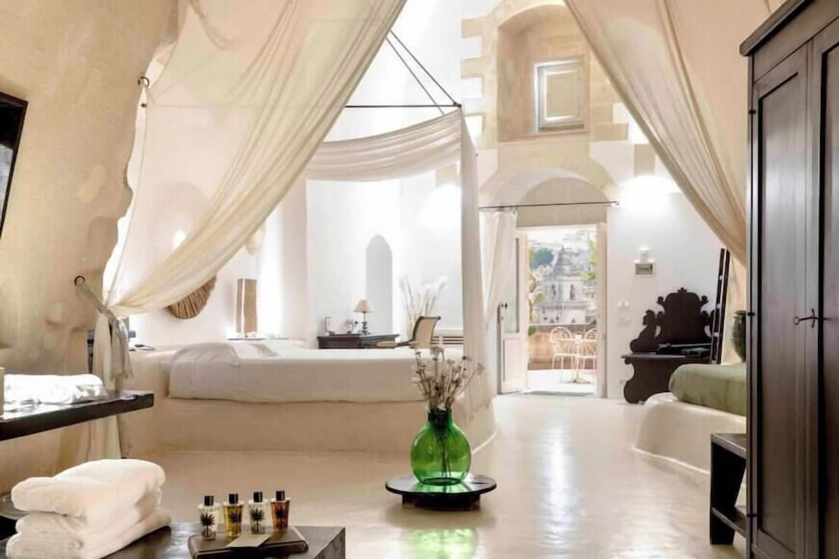 A room with a bed, a green vase, and a view of the city.