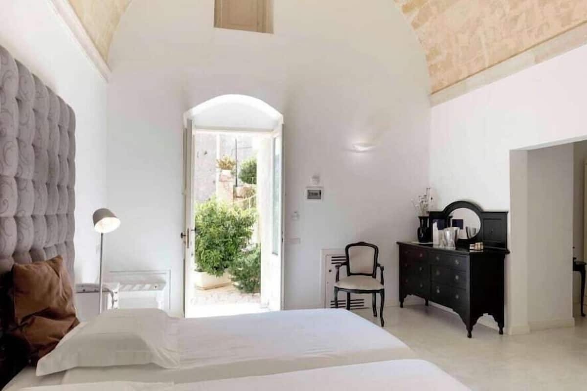 A bedroom with a bed, a dresser, a chair, and a lamp.