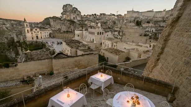 Una terraza con mesas dispuestas para comer, con vistas a un pueblo histórico de edificios de piedra y una iglesia destacada.