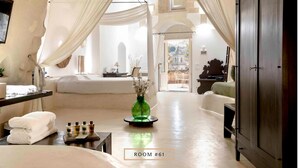 Una habitación amplia con una cama, un tocador con artículos de aseo, un florero verde y vistas a un edificio a través de un arco.