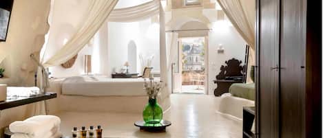 Una habitación amplia con una cama, un tocador con artículos de aseo, un florero verde y vistas a un edificio a través de un arco.