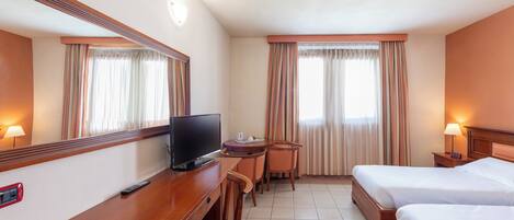 A hotel room with two beds, a desk with a TV, a chair, a small table, and a lamp.