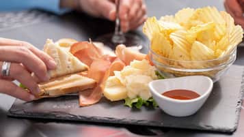 Un plateau repas composé de pain, de fromage, de jambon, de chips et d’un petit bol de sauce, le tout présenté sur une ardoise.