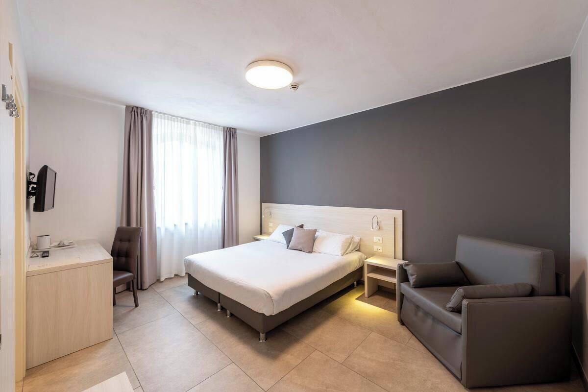 A modern hotel room with a large bed, a desk, a chair, and a sofa.