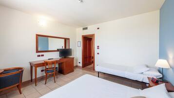 Una habitación de hotel con cama, escritorio y silla, televisor y mesita de noche con lámpara.