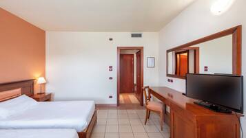 Ein Hotelzimmer mit zwei Betten, einem Schreibtisch mit Fernseher, einem Sessel, einer Lampe und einem großen Spiegel.