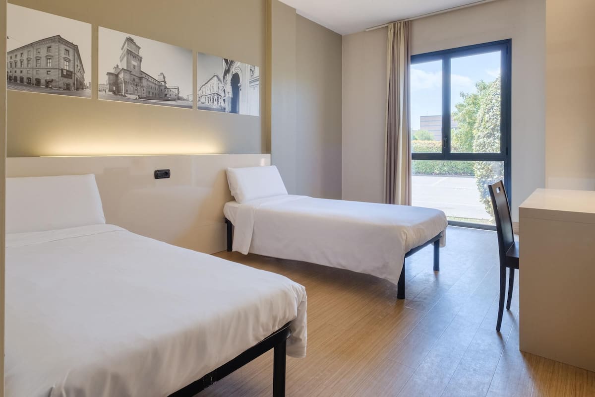 A hotel room with two beds, a desk, and a large window with a view.
