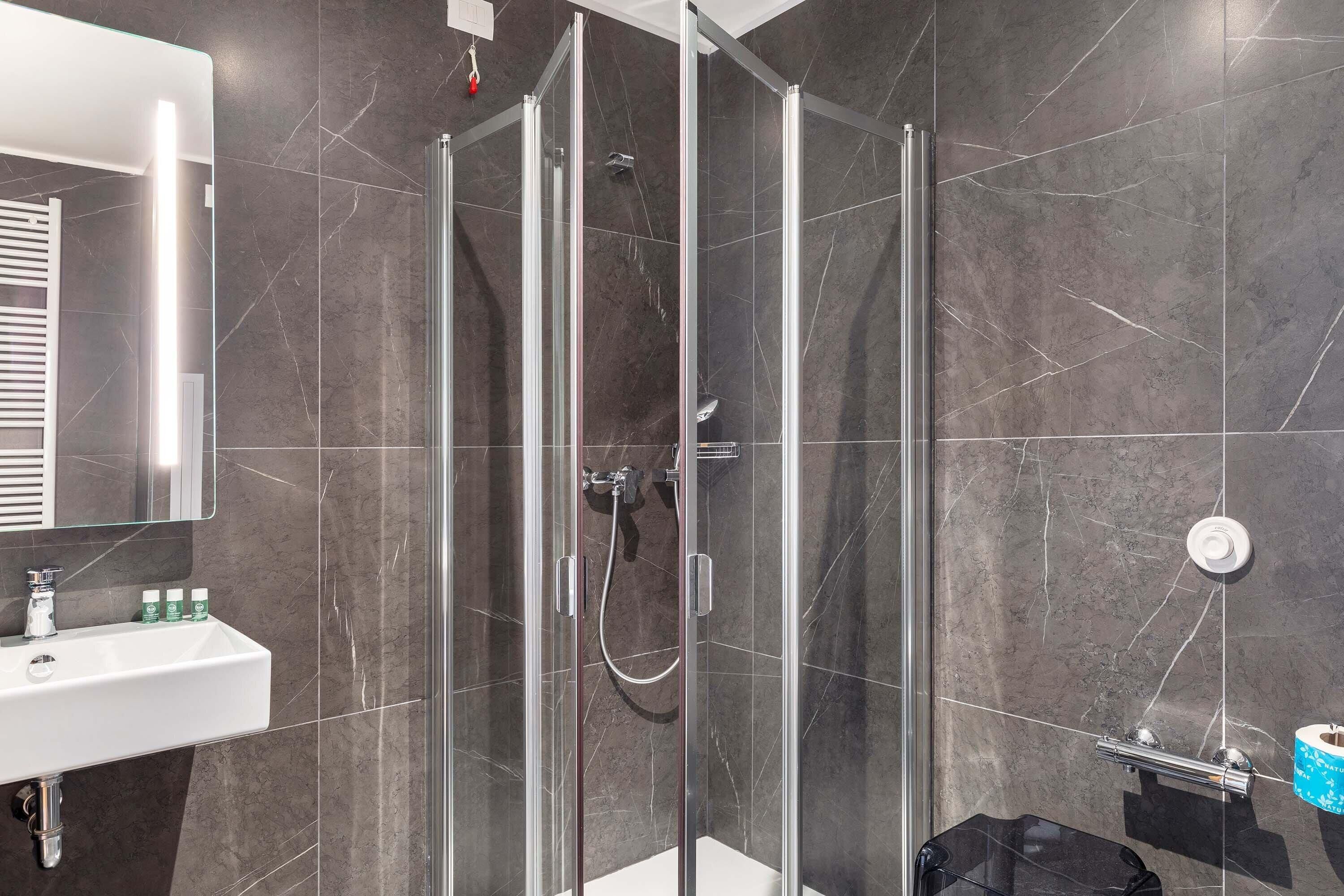 Un baño moderno con ducha de vidrio, lavamanos blanco y un espejo grande.