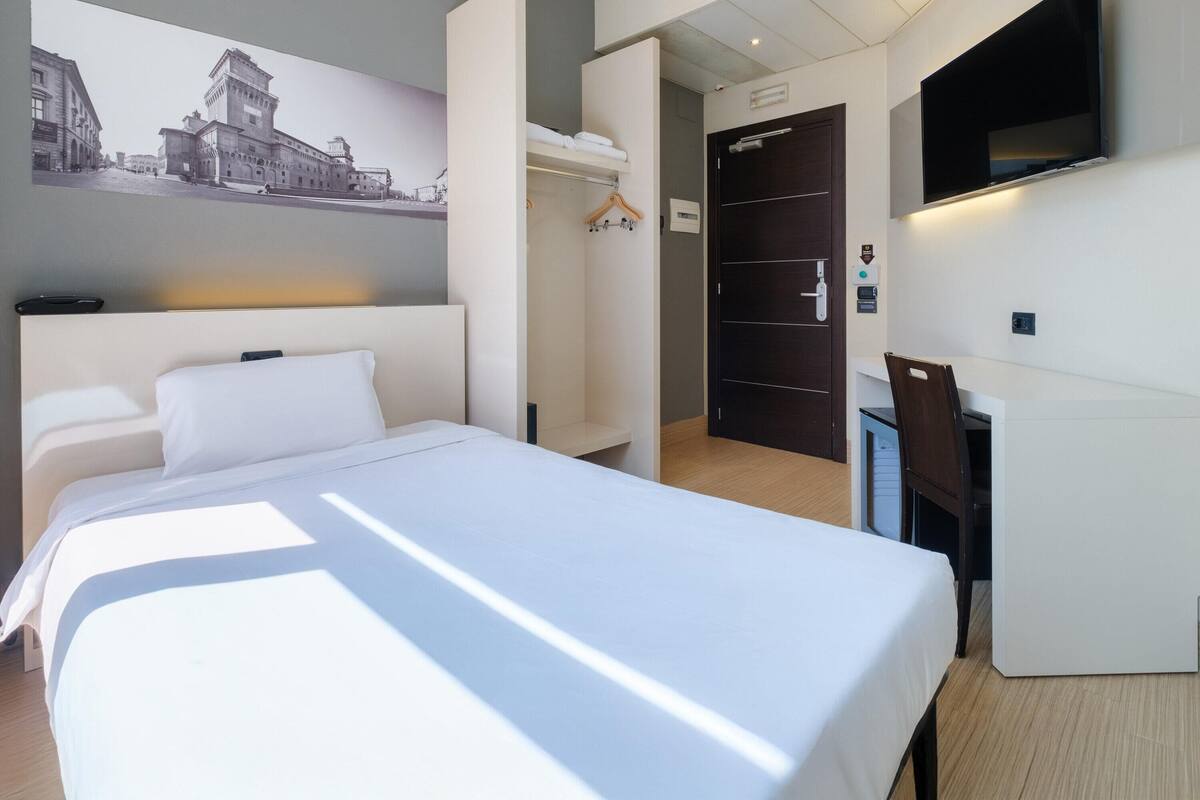 A hotel room with a large bed, a desk, a wardrobe, and a television.