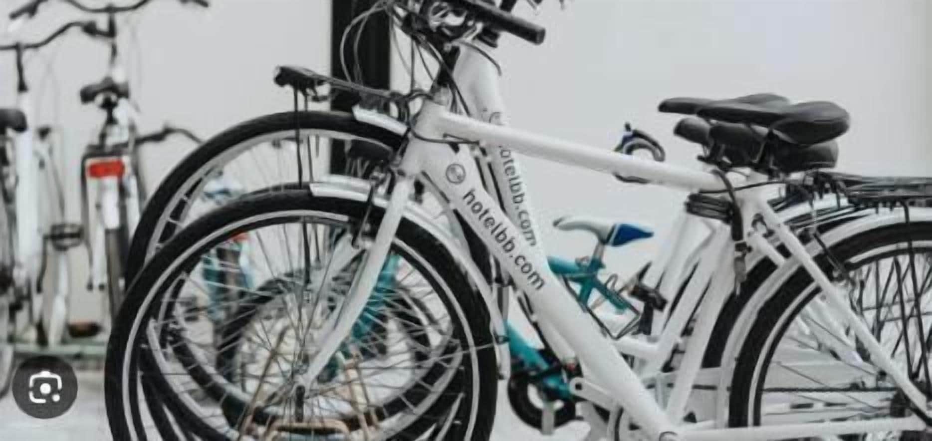 Een witte fiets met een waterfles en een helm, vastgemaakt aan het frame, geparkeerd tussen andere fietsen.