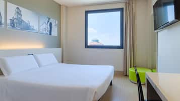 Une chambre d’hôtel avec un lit, une télévision, une fenêtre donnant sur un beau paysage et un fauteuil vert.