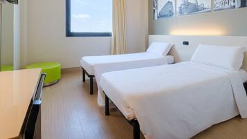 A hotel room with two single beds, a desk, a green stool, and a window with a view of buildings.