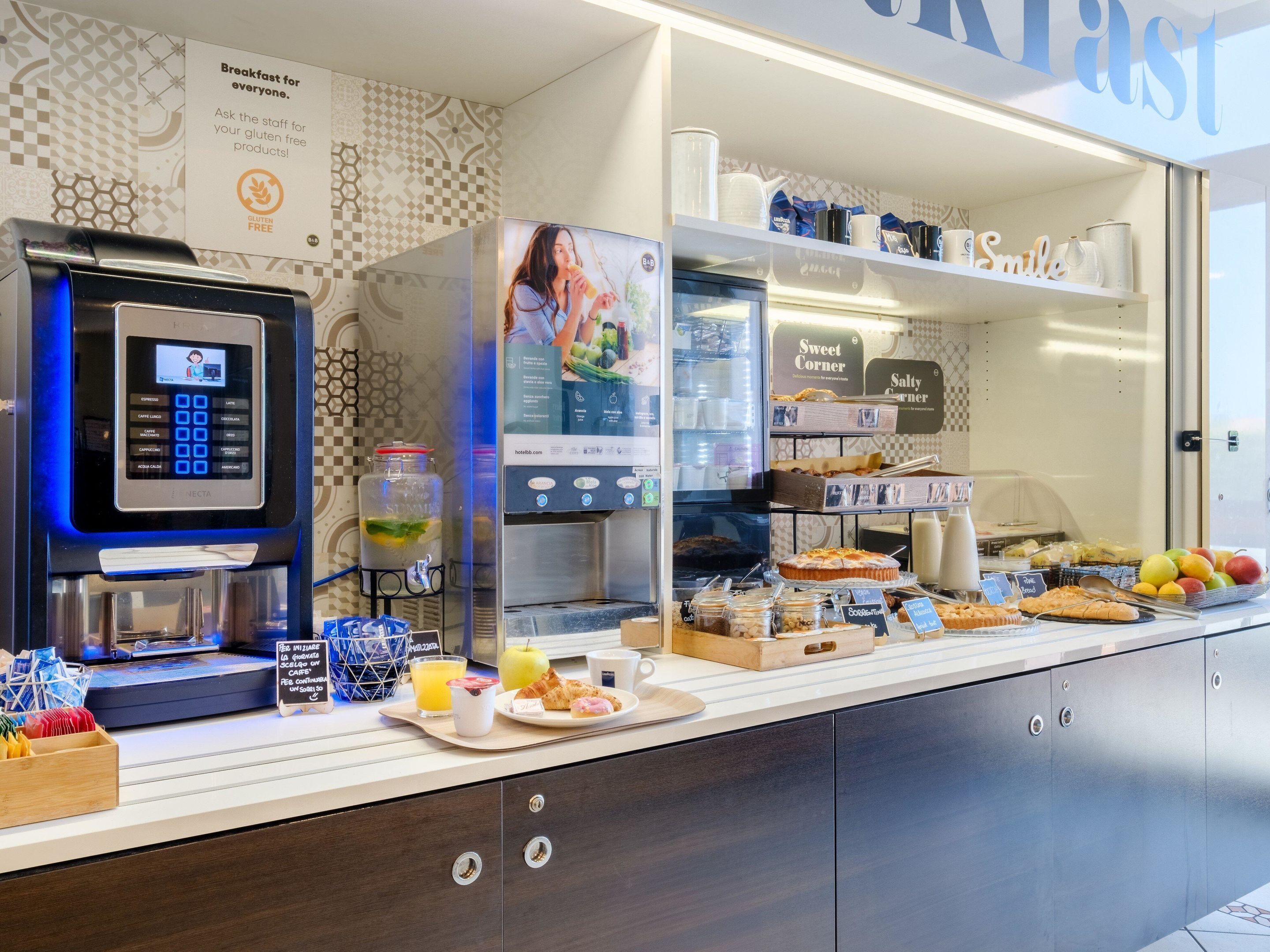 Un buffet de petit-déjeuner comprenant une machine à café en libre-service, un présentoir réfrigéré et divers aliments.